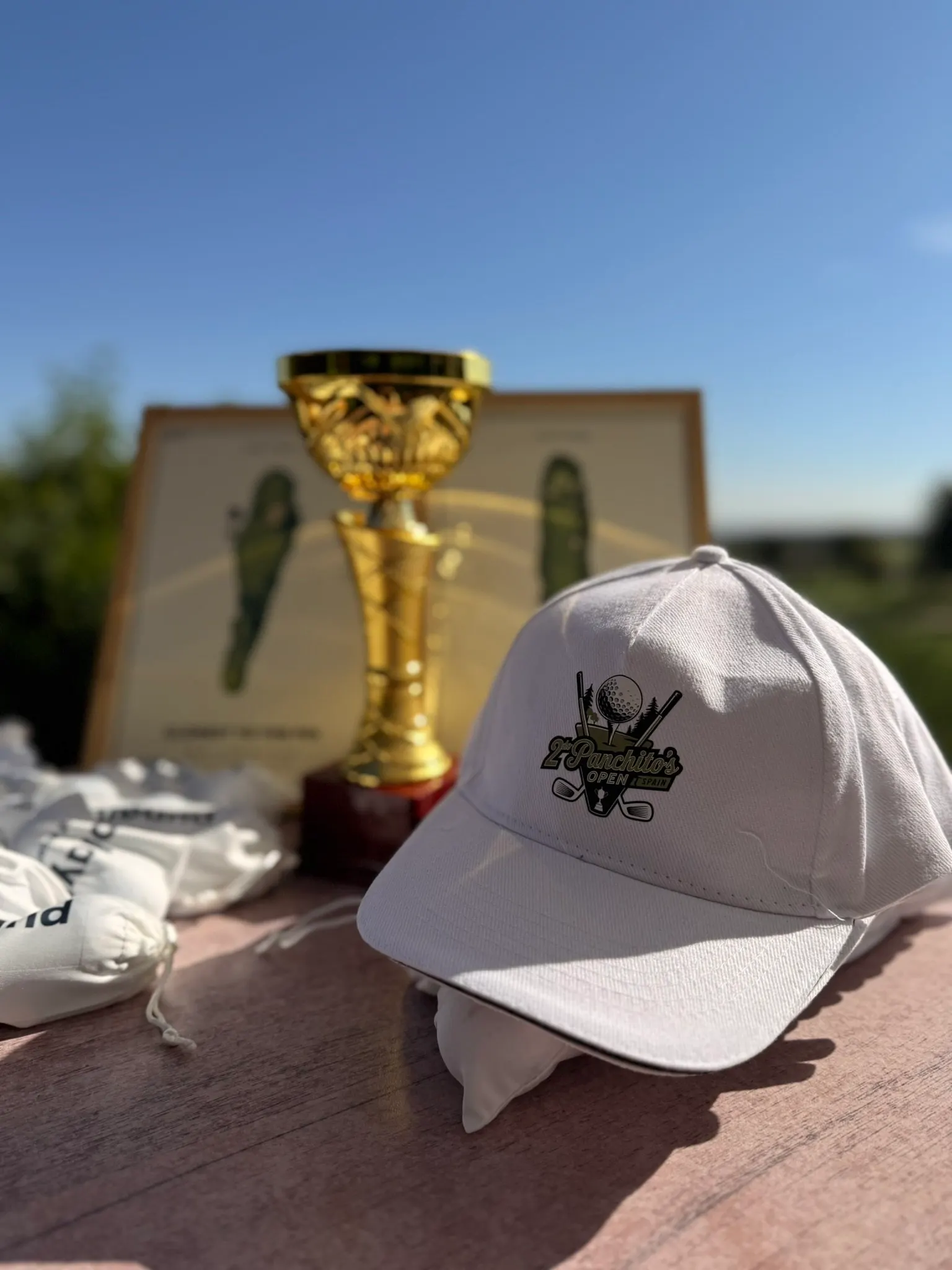 White cap printed with a custom tournament logo, next to the trophy and course prints on the prize table