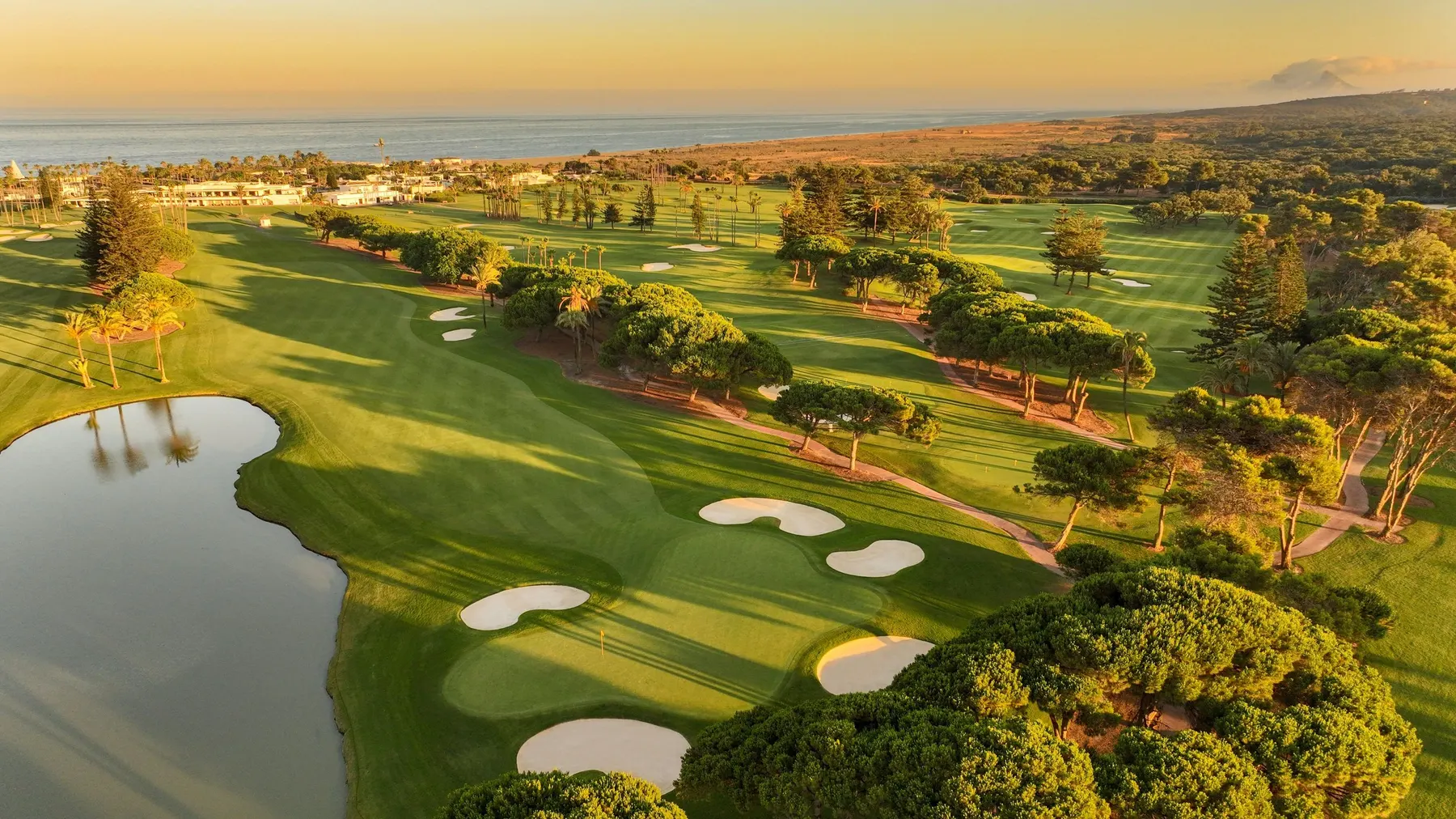 Aerial view of a coastal golf course in Sotogrande, Spain, with a lake in front of the green at sunset