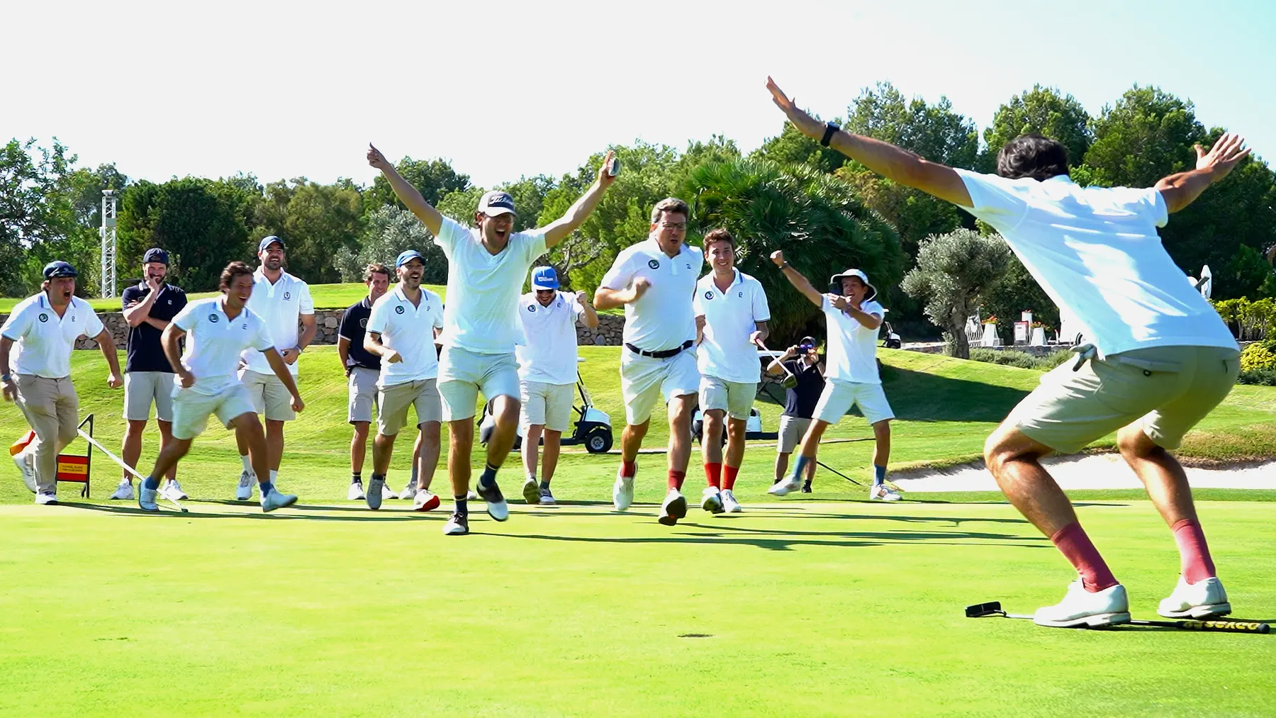 A group of golfers in team polos running onto the green to celebrate a winning putt during a playground tournament