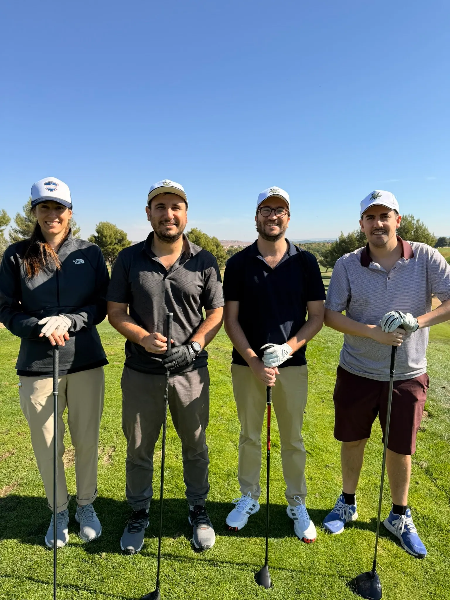Borja and three friends holding their clubs on a golf course under a blue sky