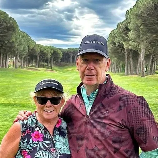 Kimberly and her partner in golf caps on a tree-lined golf course in Spain