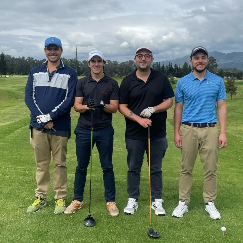 Samuel and three friends smiling on a golf course with mountains behind them