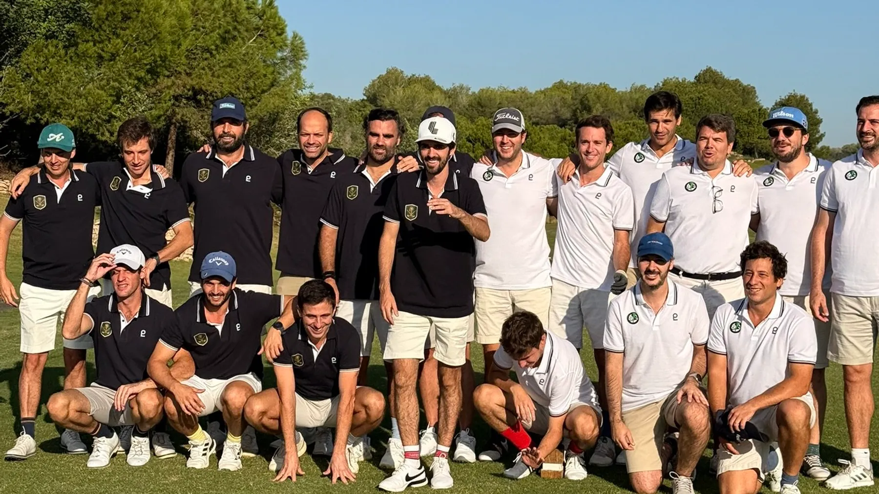 Two playground teams, one in navy polos and one in white polos, posing together on the course after a Ryder Cup style tournament in Spain